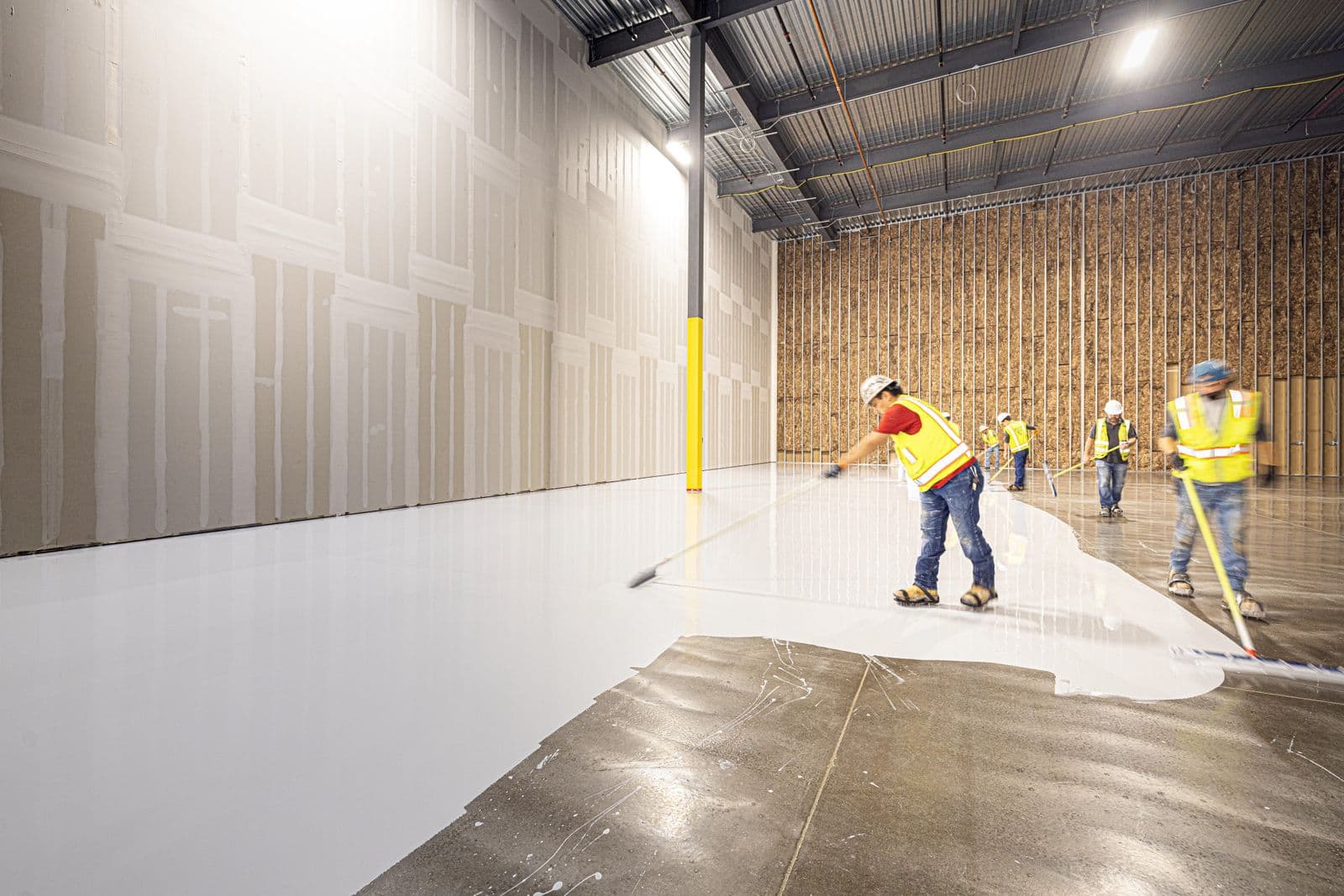 Installers applying a floor coating with squeegees and rollers during an installation
